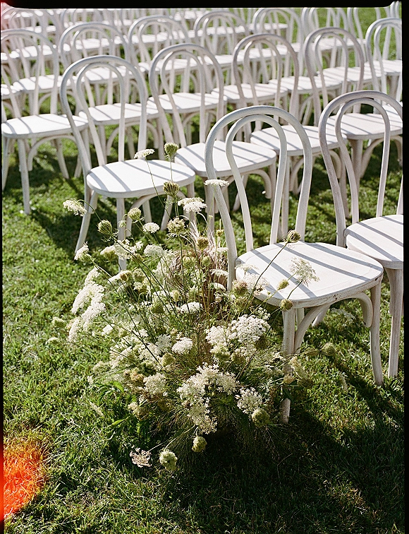 Ceremony seating with outdoor wedding chairs, white bentwood chairs in neat rows lining a grassy lawn aisle with wildflower florals
