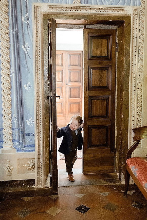 Ring bearer in a ring bearer outfit wearing a toddler suit and tie, standing by an ornate doorway in a vintage interior hallway