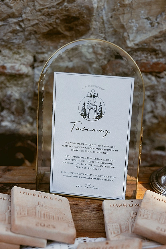 Wedding favor sign on a wooden table in an acrylic sign holder, with terracotta wedding favors arranged before a stone wall backdrop
