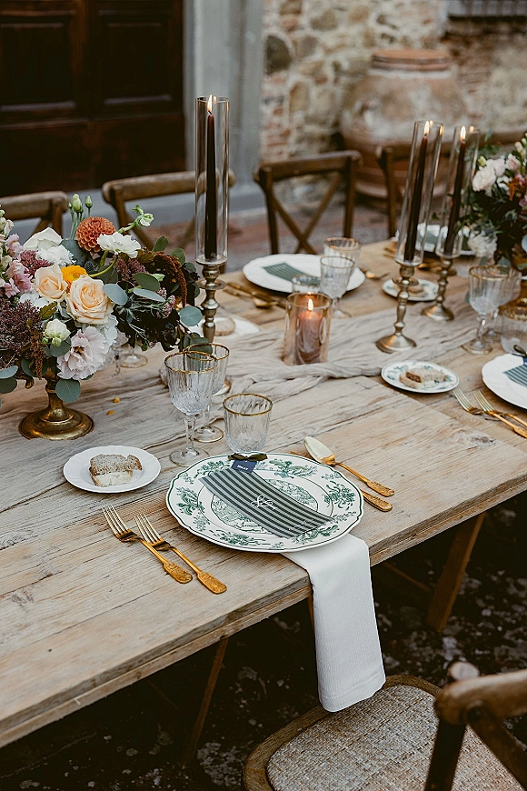 Reception tablescape with rustic wedding table setting on a wood farm table, roses and eucalyptus centerpiece, taper candles, stone wall backdrop