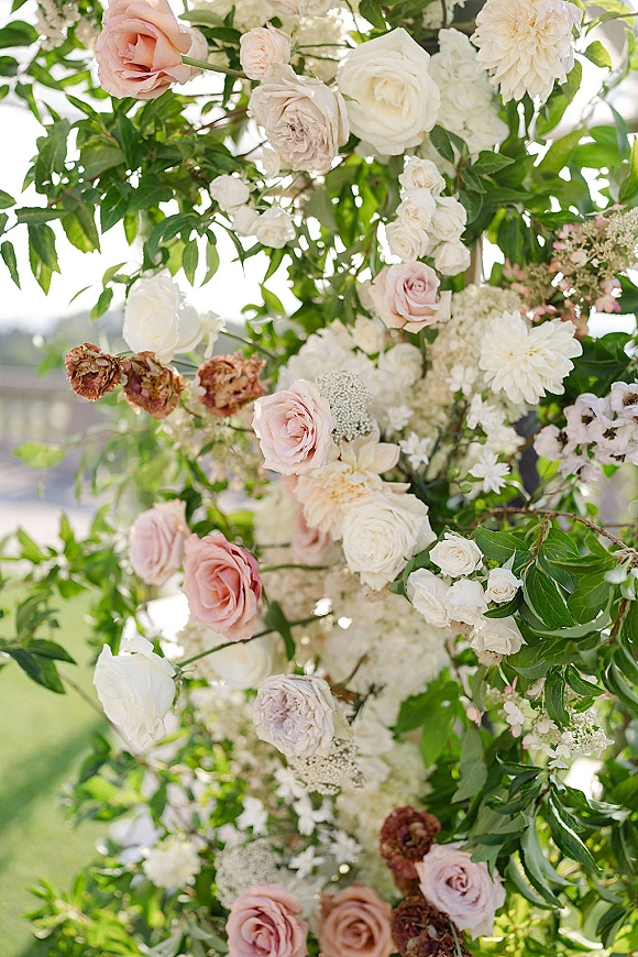 Wedding floral arch with ceremony arch flowers in roses, hydrangeas, dahlias and greenery, set on an outdoor lawn in natural light