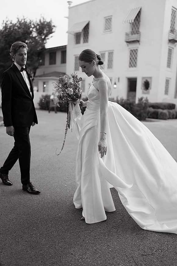 Couple portrait in a black and white wedding portrait, bride holding bouquet with long train beside groom in tux outside hotel awnings
