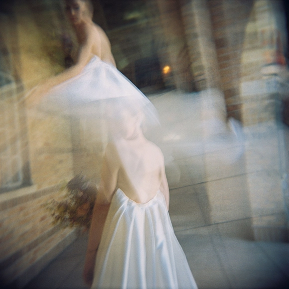 Bridal portrait of a bride with veil over her face, wearing a strapless wedding dress in an arched brick walkway with stone floor