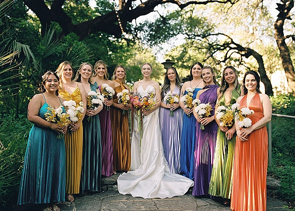 Bridesmaid group photo of the bride with bridesmaids in colorful dresses holding white and yellow bouquets on a garden stone path