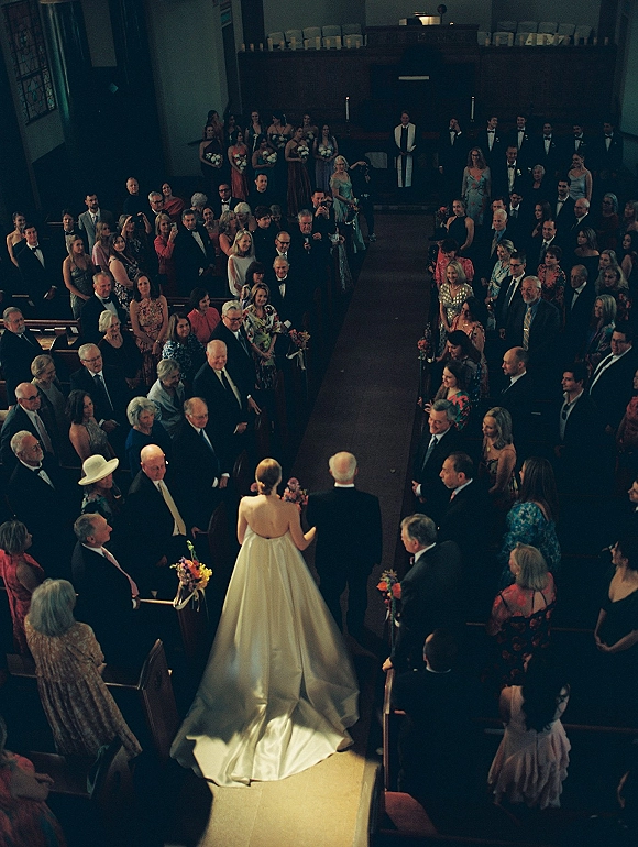 Wedding processional as the bride walking down aisle with her father, long train flowing past pews toward altar and stained glass window