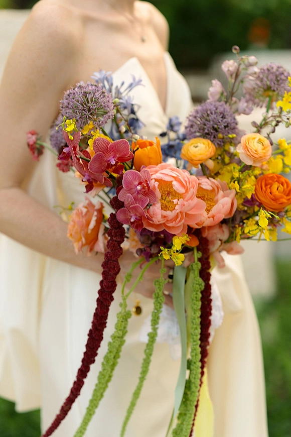 Bridal bouquet with colorful bridal bouquet blooms of orchids, ranunculus, peony and allium, trailing greenery and ribbon on a lawn