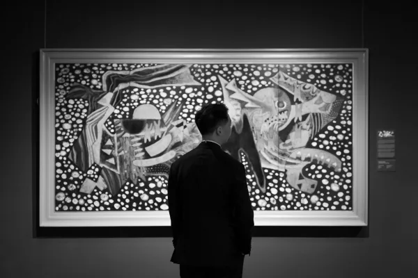 Groom portrait in tuxedo, seen from behind as he studies framed artwork in an art museum gallery beside an exhibit label.