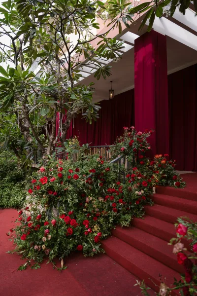 Ceremony aisle decor with red rose aisle flowers lining a red carpet runner, greenery garlands on stairs, and burgundy draping by lantern light