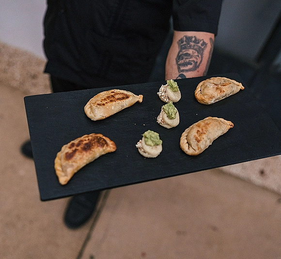 Wedding appetizers on a black serving tray, passed hors d'oeuvres with mini empanadas and bite-size canapes, held by a server on patio pavement
