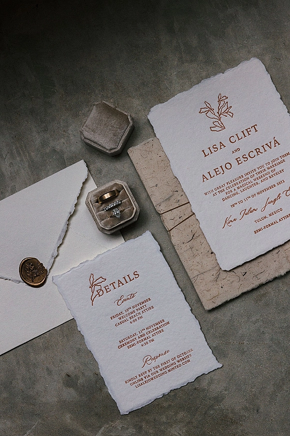 Wedding invitation suite with deckle edge wedding invitations, wax seal and rings in a hexagon box arranged on a stone surface