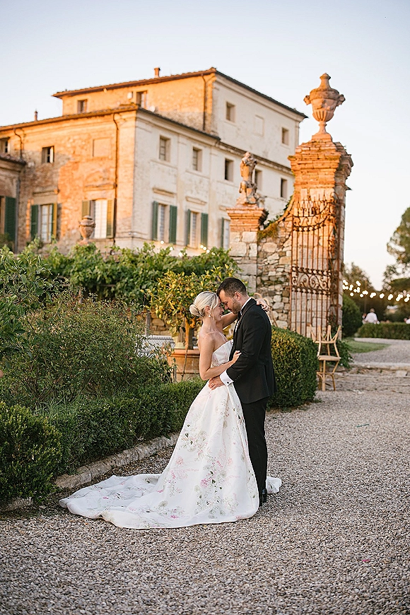 Couple portrait of bride and groom embrace with a forehead touch by a wrought iron gate, bride in strapless gown and tuxedoed groom