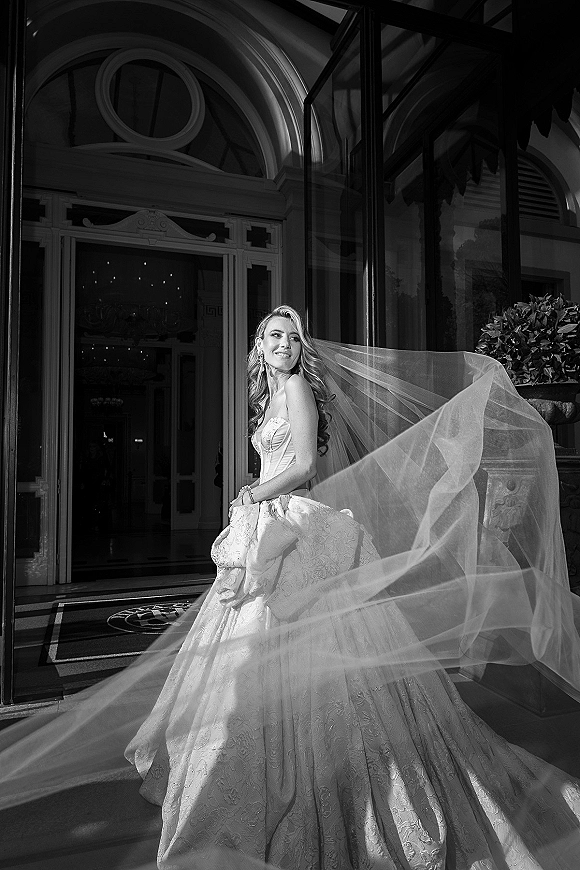 Bridal portrait of a bride in a strapless lace ball gown with a long veil and drop earrings on stone steps by an arched doorway