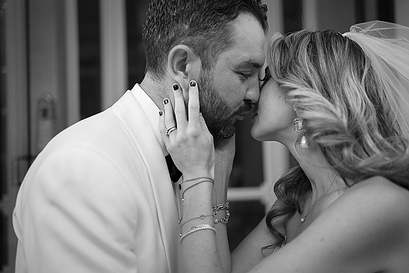 Wedding kiss portrait of bride and groom kissing close up in a doorway, bride’s hand on his face showing engagement ring and veil