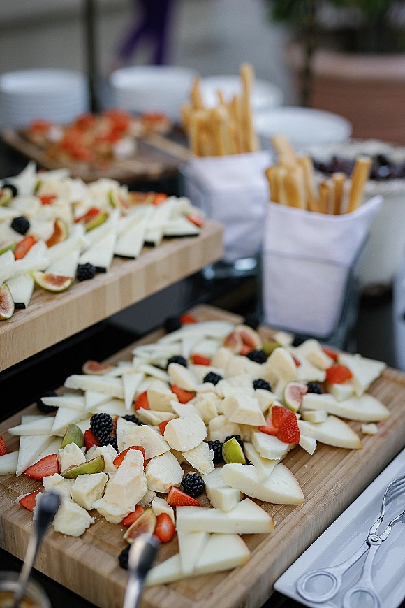 Wedding cheese board with brie slices, strawberries, blackberries, figs and breadsticks on wooden boards, set on a glass buffet table