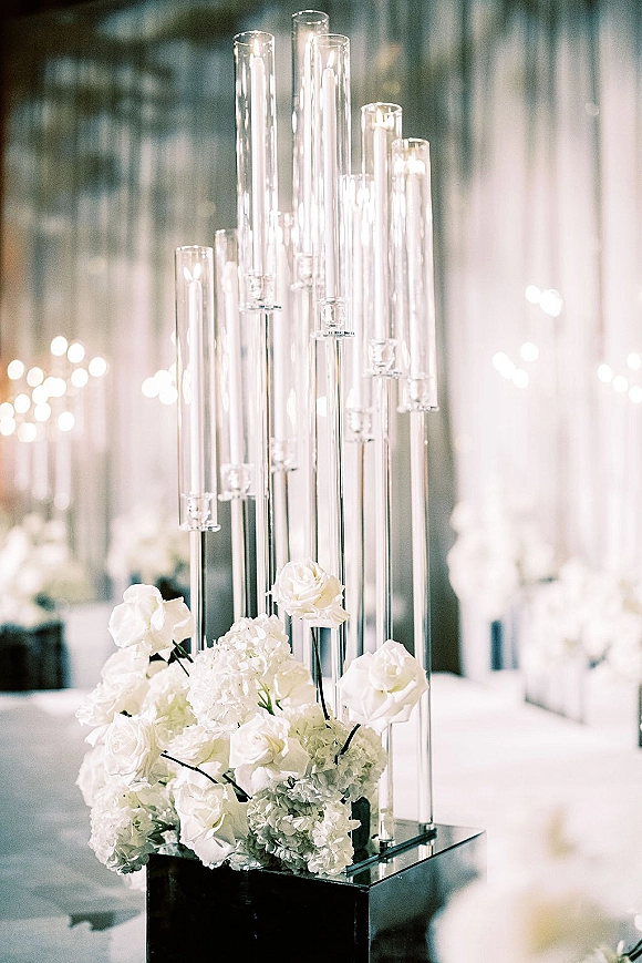 Wedding centerpiece with a tall glass candle centerpiece, pillar candles, white roses and hydrangea on a reception table in soft lights