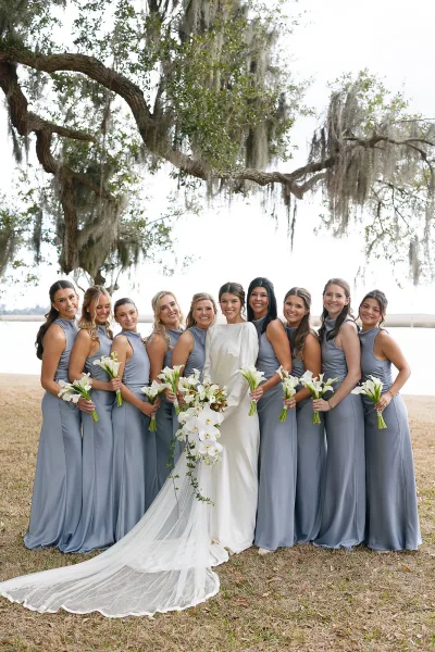 Bridesmaid group photo with bride and bridesmaids in satin dresses holding calla lily bouquets under an oak tree with Spanish moss by water