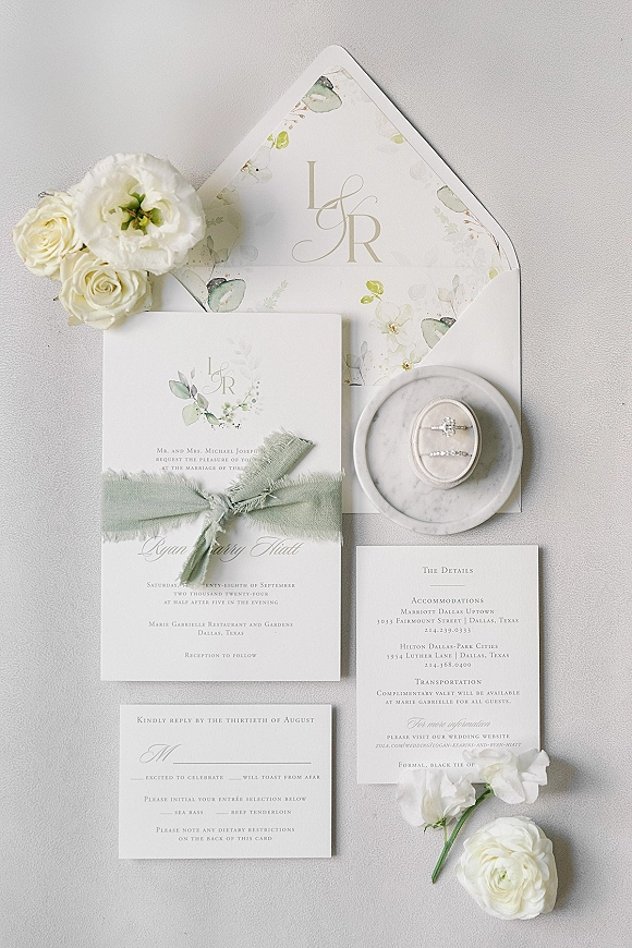 Wedding invitation suite wedding stationery flat lay with monogram cards, silk ribbon, ring box and bands on light gray fabric backdrop