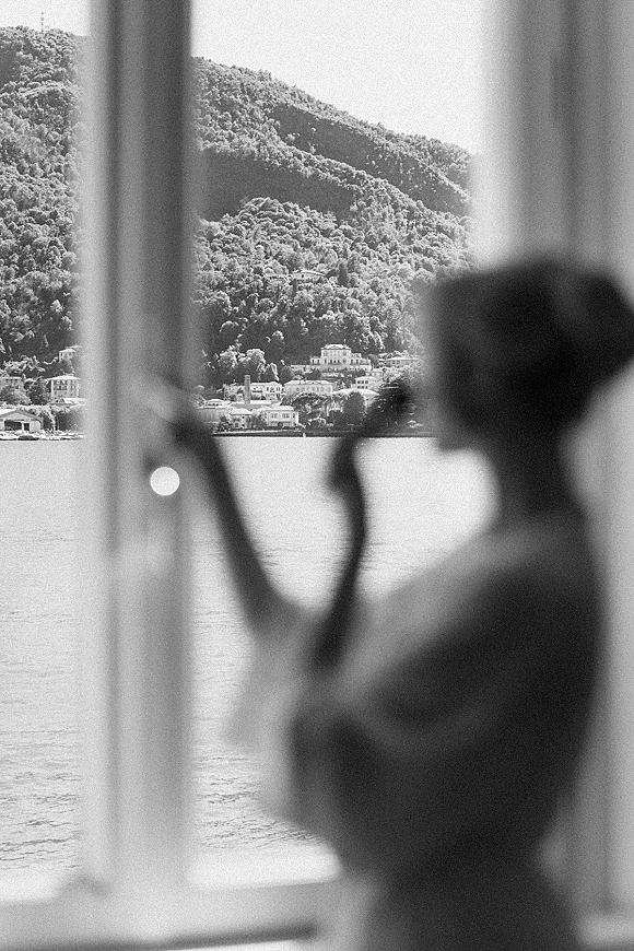 Wedding silhouette portrait of a bride at window, her wedding veil softly outlined as she gazes over a lake and mountains beyond
