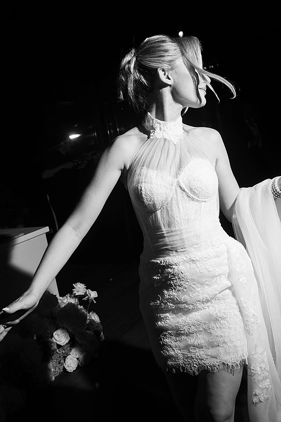 Bridal portrait of a bride in a lace wedding dress with veil and rose bouquet, side profile by a car door in night lighting