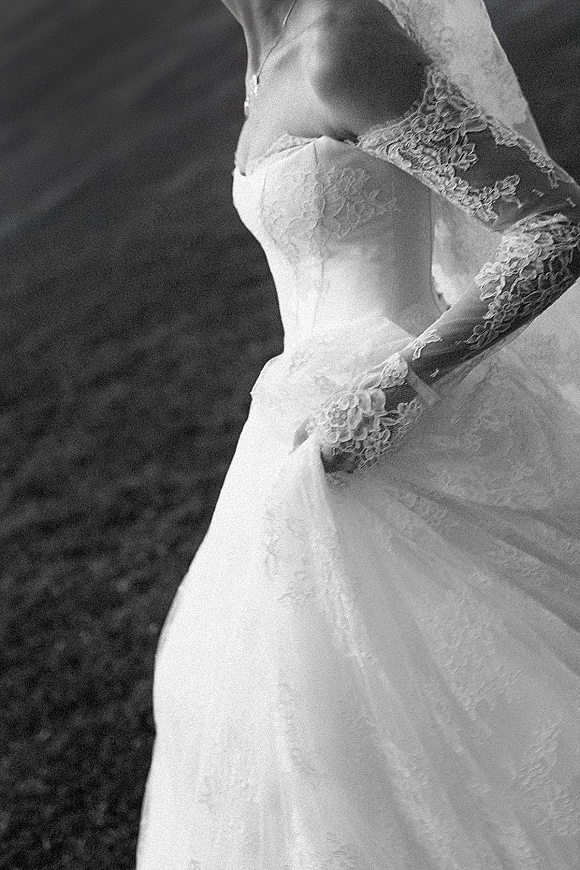 Wedding dress with a lace wedding dress bodice, illusion sleeves, veil, and tulle skirt laid across a grass lawn with a necklace
