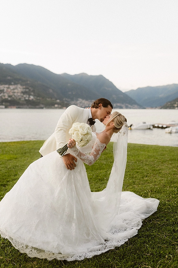 Wedding kiss portrait of bride and groom in a dip kiss wedding photo, lace veil flowing by a mountain lake with dock and boats behind