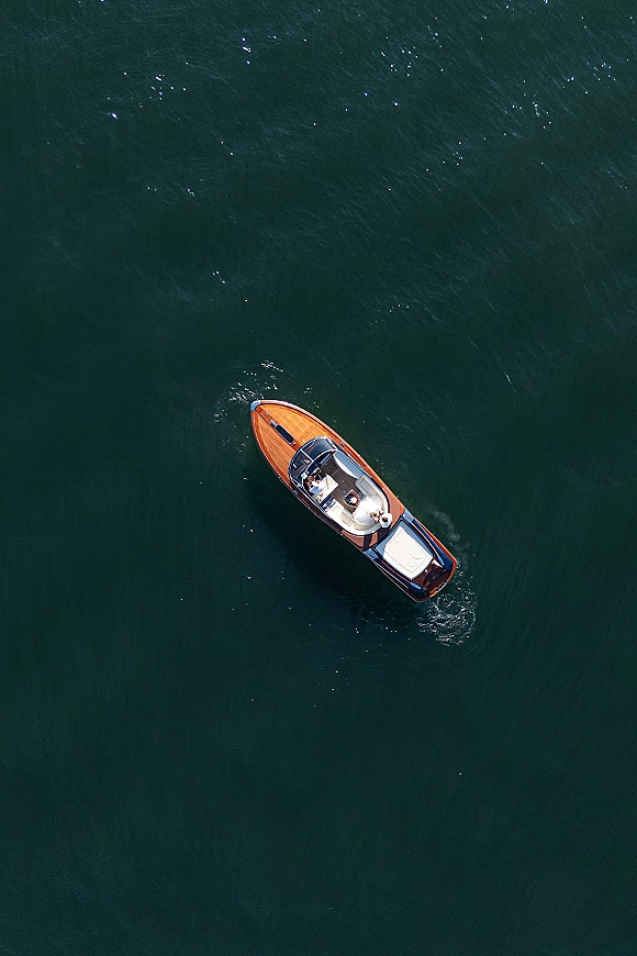 Boat wedding portrait of a bride and groom on boat in a classic wooden speedboat, groom driving as wake ripples trail on open water