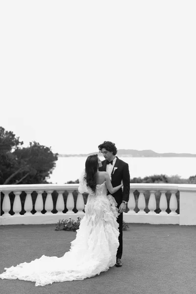 Couple portrait in a black and white wedding portrait as bride and groom embrace on a stone terrace with ocean and hills beyond
