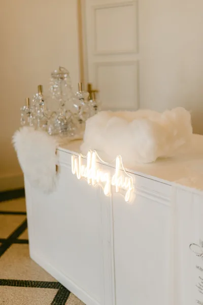 Wedding welcome sign with wedding neon sign on a white cabinet, styled with crystal perfume bottles against a cream wall and paneled door