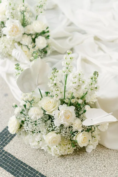 Wedding floral arrangement of white wedding flowers with roses, anthurium, hydrangea, greenery and white drape on stone tile floor