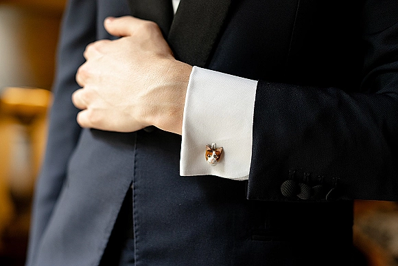 Groom cufflinks with cat cufflinks on a white French cuff shirt beneath a black tuxedo jacket, close-up of whimsical wedding accessory detail