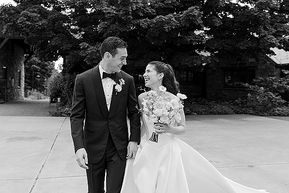 Couple portrait, black and white wedding portrait of bride and groom walking and laughing on a tree-lined driveway, bride holding bouquet