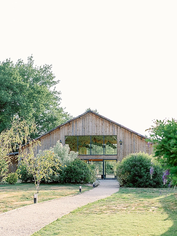 Barn wedding venue with a rustic barn exterior, glass doors and large windows along a gravel walkway with path lights, set by lawn and trees
