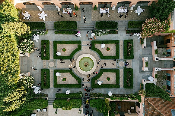 Cocktail hour setup with wedding cocktail hour tables draped in white linens beside a courtyard fountain, buffet platters in formal gardens