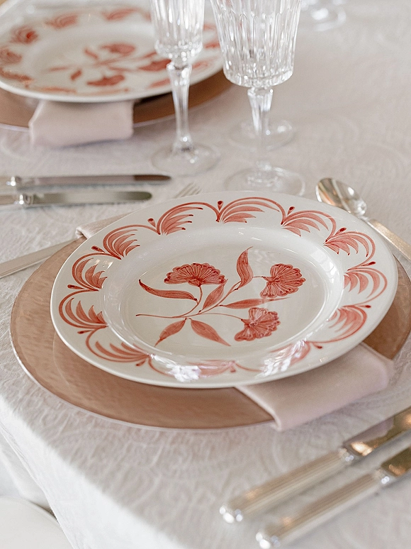Wedding tablescape with wedding place setting featuring floral china, blush napkin, silver flatware, and champagne flutes on white linen table
