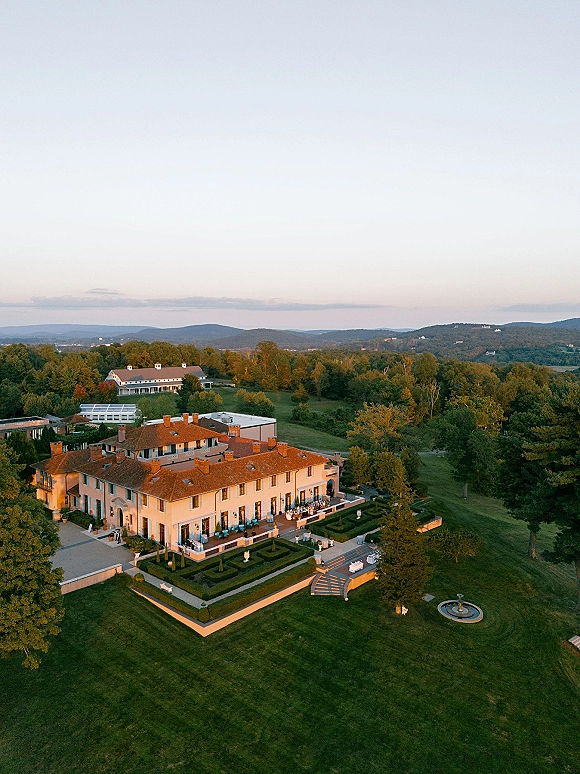 Wedding venue aerial view of a grand estate wedding venue with a mansion terrace, hedges, garden steps, and a fountain on rolling hills
