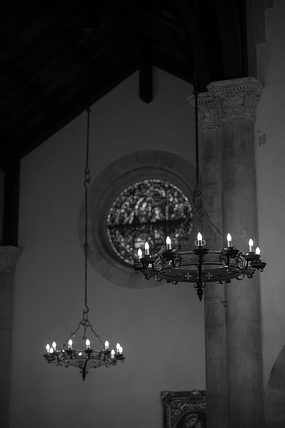 Church chandeliers in a wedding church interior with candle-style bulbs hanging from chains near a stone column and stained glass window