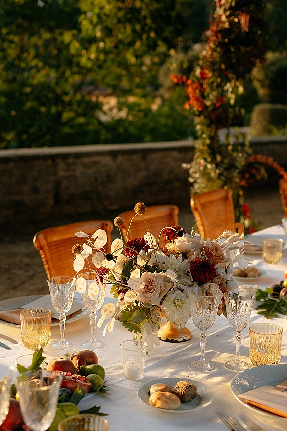 Reception tablescape with outdoor reception table styling, white linen, rose and dahlia centerpiece, taper candles, crystal glassware, fruit in a garden setting