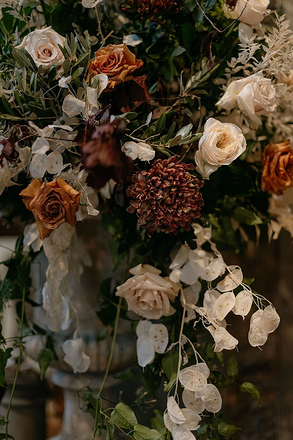 Wedding floral arrangement of roses and dahlia with white lunaria on a grounded floral installation against a soft indoor backdrop