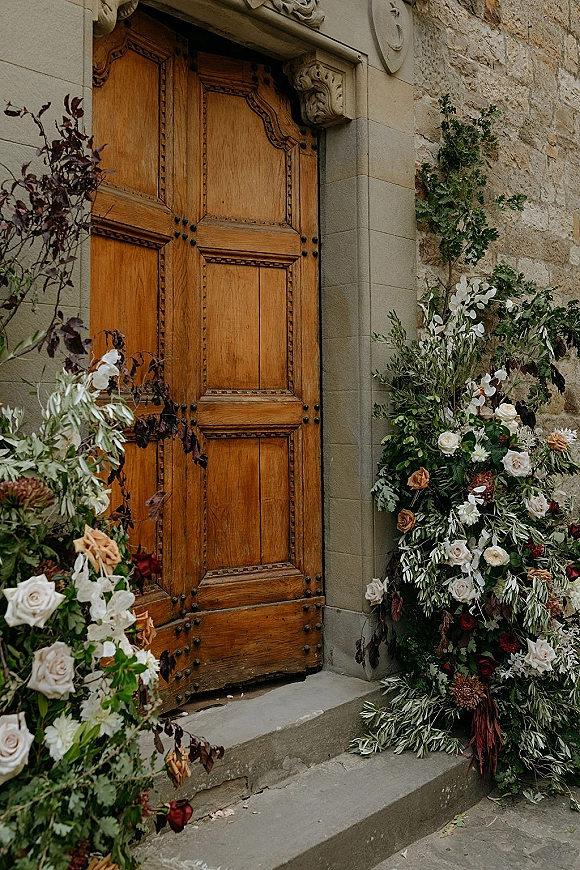 Wedding entrance decor with wedding door flowers, lush roses and greenery framing wooden doors on stone steps by a stone wall
