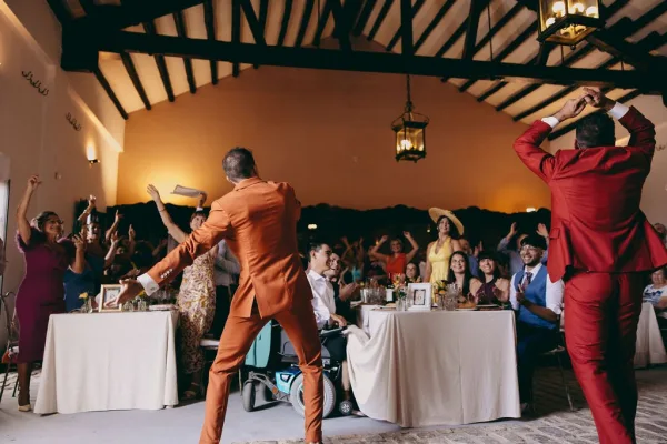 Reception dance at a wedding reception party as guests twirl beneath a wood-beam ceiling, with warm lanterns aglow above the cobblestone floor.