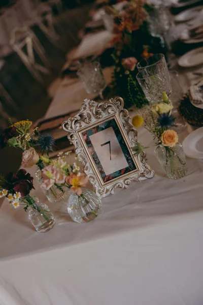 Wedding table number displayed as a framed table number, with bud vases adding a gentle flourish along the tabletop.