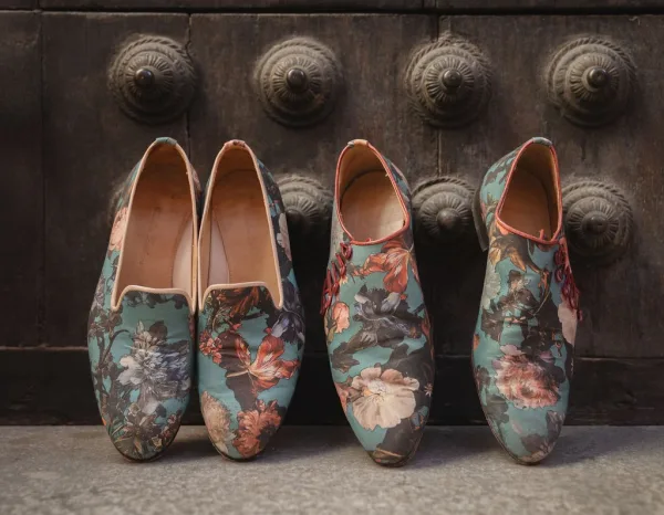 Groom shoes with a floral print on a weathered stone floor, set against a wood door with metal studs.