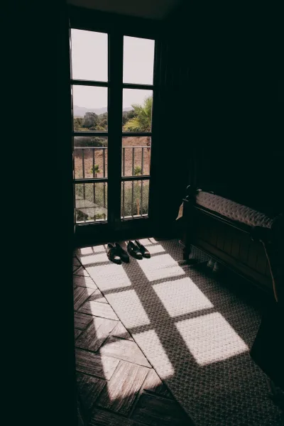 Wedding shoes, classic groom shoes arranged by French doors, with a balcony railing and palm-dotted hillside landscape beyond.