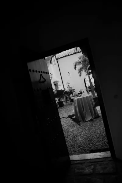 Cocktail table setup for a wedding cocktail hour, draped in table linen, set in a courtyard with cobblestone floor, stucco walls, and a palm tree.