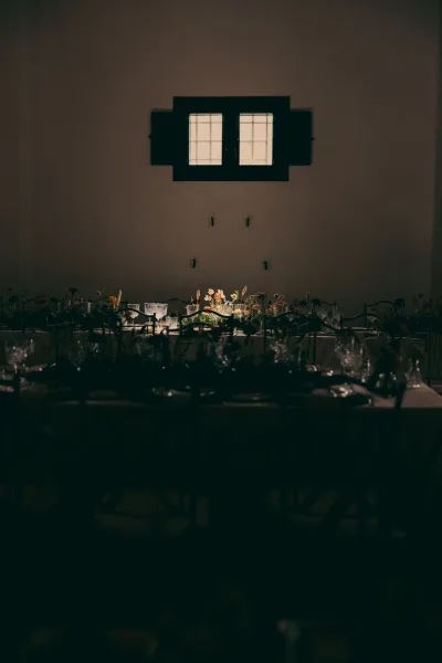 Reception tablescape featuring long banquet table decor, styled with floral centerpieces, set in an indoor room with windows and wall sconces.