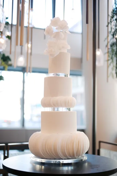 Wedding cake with modern wedding cake styling, white ruffled fondant tiers and wafer paper flowers on clear acrylic separators by windows