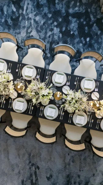 Reception tablescape with black tablecloth wedding table, white plates, menu cards, silver flatware, stemware, and gold lamps on blue carpet