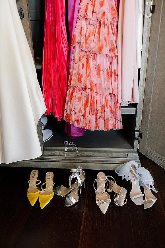 Wedding shoes and bridal heels arranged on a wood floor in a closet, featuring strappy sandals and pointed toes with bow detail