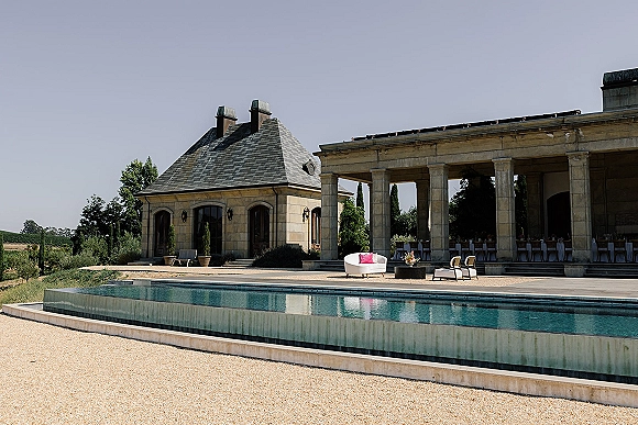 Wedding venue exterior with luxury wedding venue poolside lounge, white sofa and floral centerpiece set beside a stone colonnade courtyard