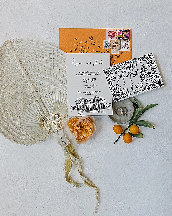 Wedding invitation suite with hand drawn wedding invitation, RSVP card, rings and citrus branch on a white flat lay with ribbon accent